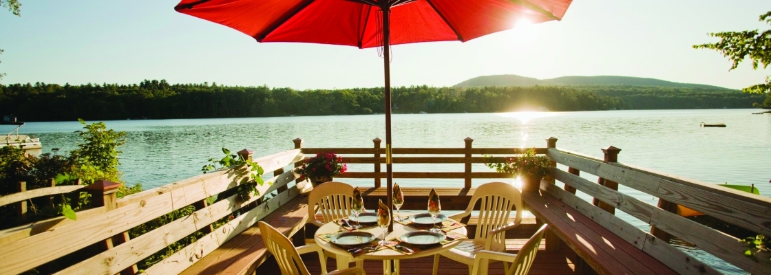 A big deck with a dining table and sun umbrella on the lake